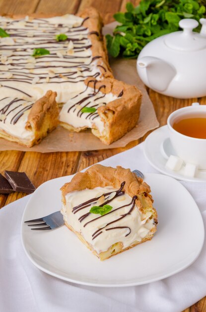 Tarta de crema casera con crema pastelera y crema bávara con glaseado de chocolate, pétalos de almendras y hojas de menta en la parte superior sobre una superficie de madera oscura