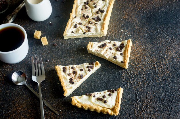 Tarta con crema de vainilla o tarta de queso con gotas de chocolate y taza de café