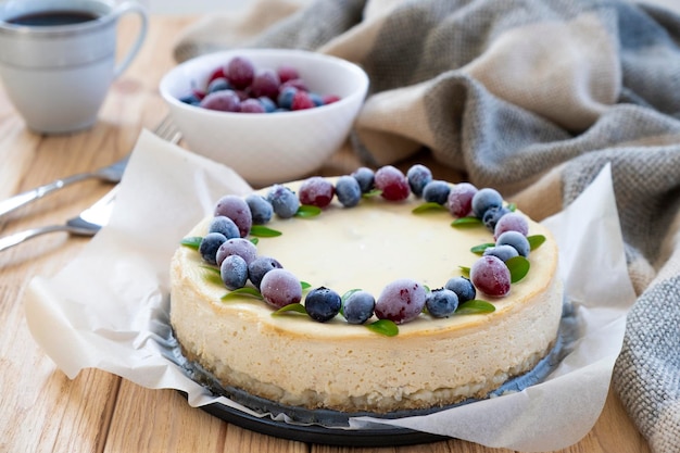 Tarta cremosa de queso mascarpone con bayas de invierno en pergamino con taza de té en el fondo Pastelería casera postre acogedor