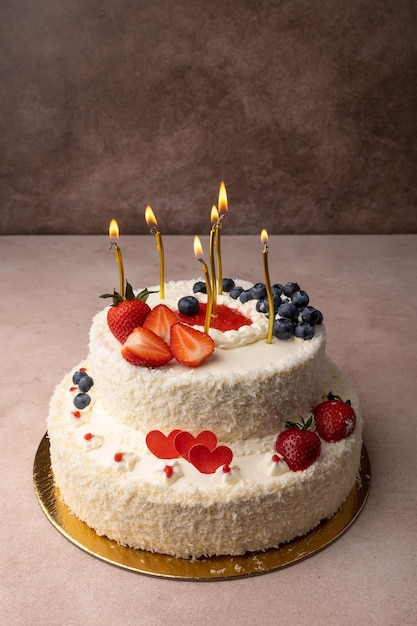 Foto tarta de cumpleaños de fresa y coco con crema y bayas frescas tarta de aniversario casera en capas con velas encendidas primer plano de enfoque selectivo