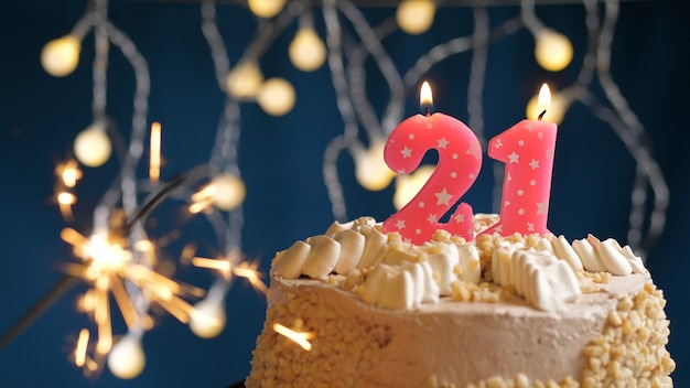 Foto tarta de cumpleaños con número 21 velas rosas y bengala encendida en backgraund azul. de cerca