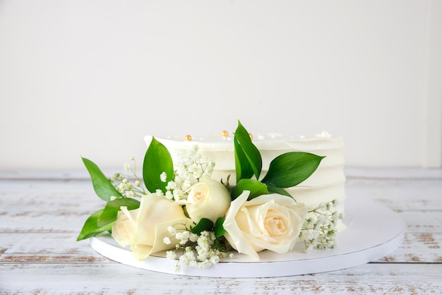 Tarta de cumpleaños con rosas blancas sobre fondo blanco de madera.