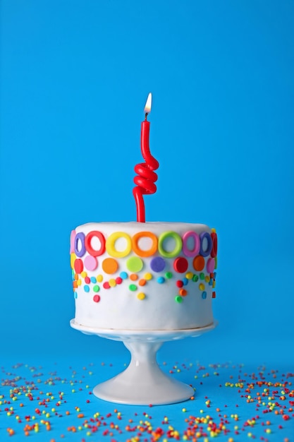 Tarta de cumpleaños con una vela sobre fondo azul.