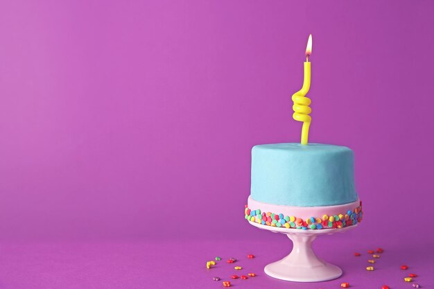 Foto tarta de cumpleaños con una vela sobre fondo morado.