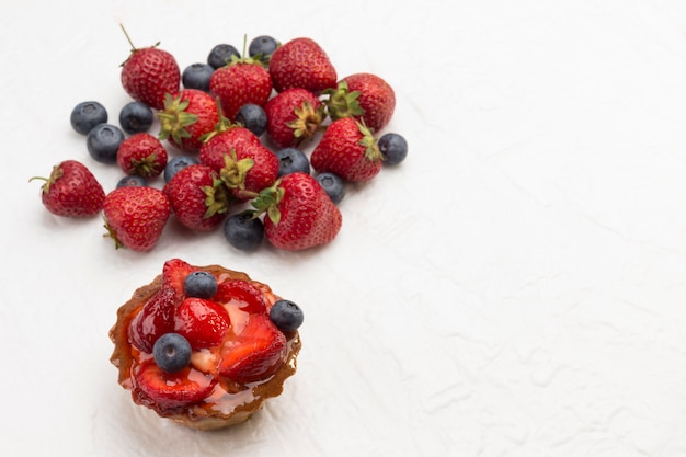 Tarta decorada con frutos rojos frescos. Fresas y arándanos sobre fondo blanco.