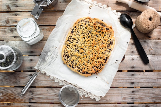 Tarta entera rallada sobre una hoja de papel pergamino rodeada de utensilios de cocina sobre una mesa de madera