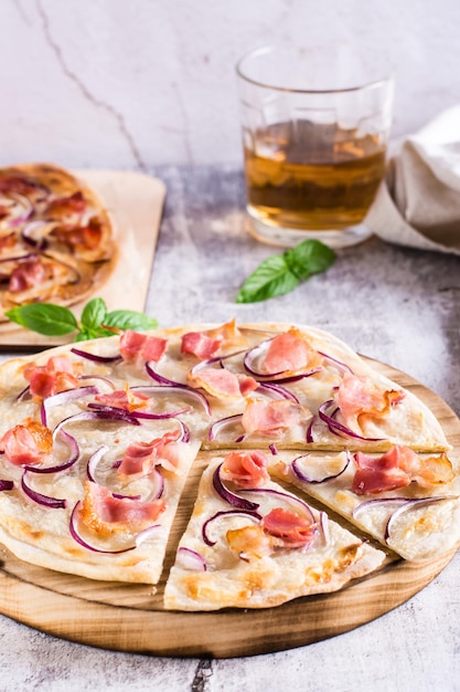 Tarta francesa flammkuchen con queso crema, cebolla y tocino en un tablero sobre la mesa Vista vertical