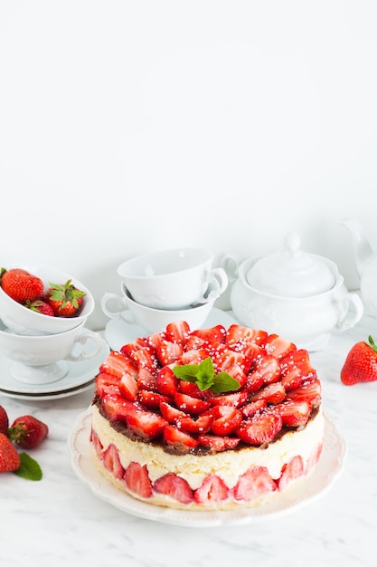 Tarta de fresa Fraisier en el plato blanco y tazas para la hora del té, bayas y vajilla en el fondo