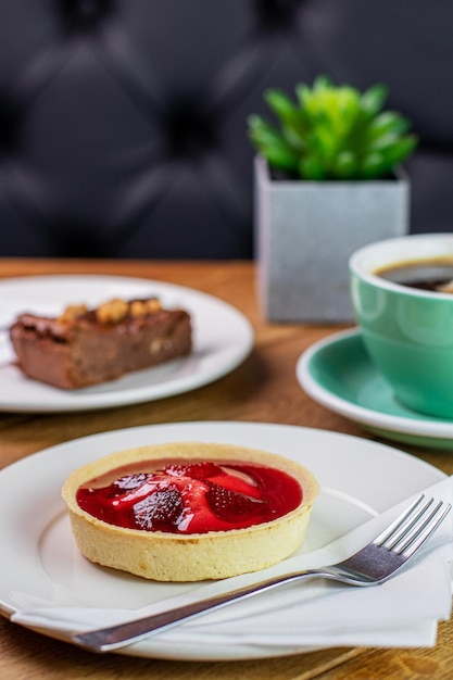 Foto tarta de fresa con una taza de café en la mesa de la cafetería y fondo oscuro