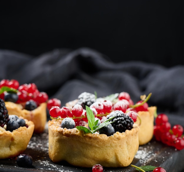 Tarta de frutas con grosellas rojas espolvoreadas con azúcar en polvo sobre una mesa negra