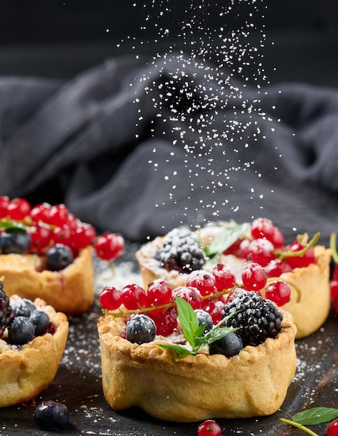 Tarta de frutas con grosellas rojas espolvoreadas con azúcar en polvo sobre una mesa negra