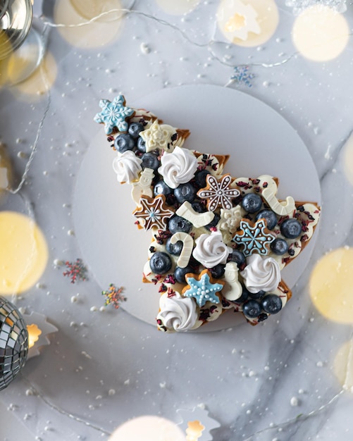 Tarta de frutas navideñas decoradas con merengue, galletas de jengibre, copos de nieve, arándanos Vertical