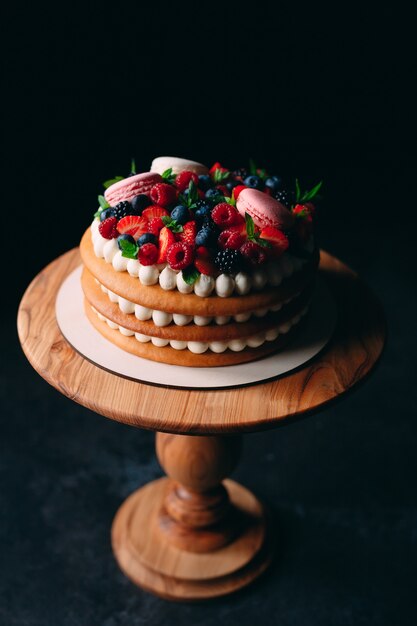 Tarta de frutas. Pastel decorado con bayas en un soporte de madera sobre un negro.