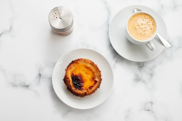 Tarta de huevo típico portugués pastel de nata con taza de café sobre fondo de cerámica