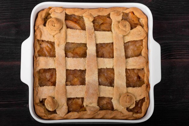 Tarta de manzana en una bandeja para hornear de cerámica cuadrada sobre un fondo de madera oscura