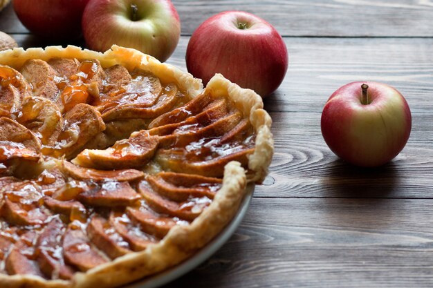 Tarta de manzana con canela, manzana fresca y salsa de caramelo en un plato sobre una mesa de madera oscura.