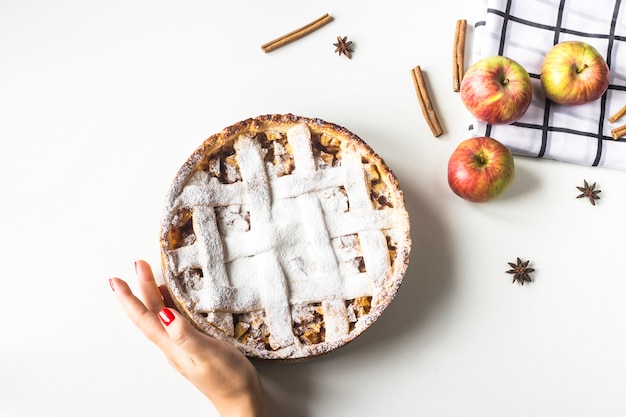 Tarta de manzana casera rociada con azúcar en polvo en mano femenina sobre una mesa blanca