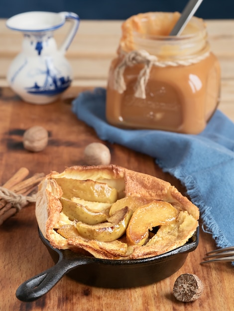 Tarta de manzana casera con salsa de caramelo en una mesa de madera. De cerca. Cerca de una jarra de caramelo, leche y especias. Sabroso postre