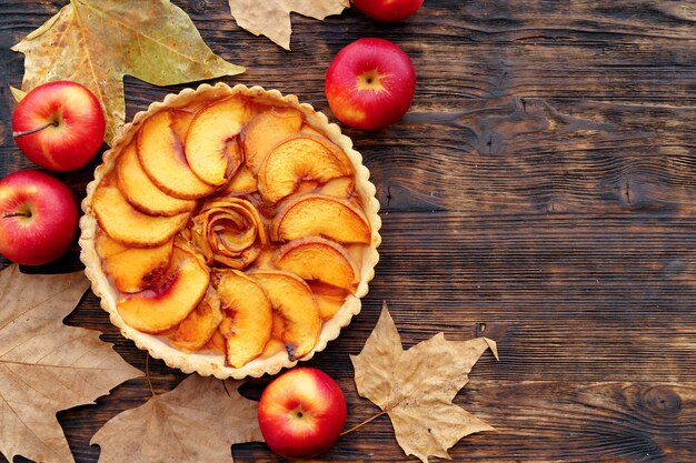 Tarta de manzana y manzanas rojas sobre mesa de madera