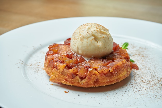 Tarta de manzana recién horneado de masa quebrada con una bola de helado en un plato blanco sobre una mesa de madera. Deliciosos pasteles de desayuno