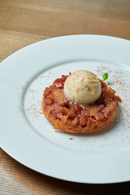 Tarta de manzana recién horneado de masa quebrada con una bola de helado en un plato blanco sobre una mesa de madera. Deliciosos pasteles de desayuno