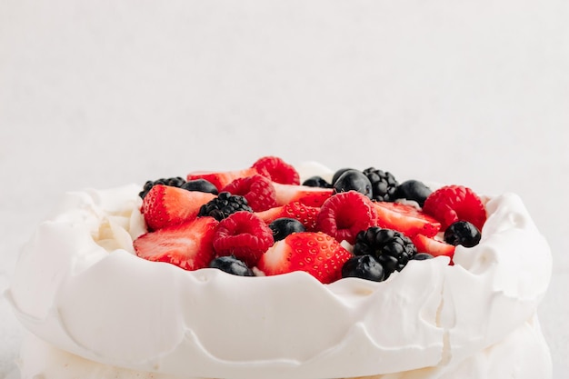 Tarta de merengue Pavlova con bayas frescas sobre fondo blanco.