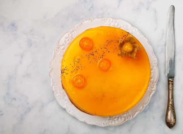 Tarta de mousse con naranja y kumquat (albaricoque, maracuyá, durazno, caqui) en un plato blanco sobre una mesa de mármol,