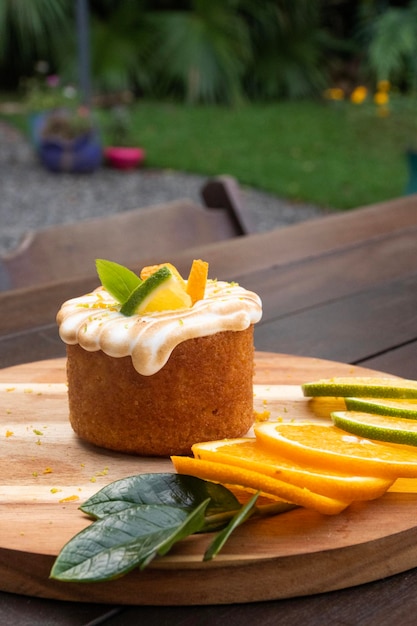 Tarta de naranja con cobertura de crema blanca tostada sobre una mesa rústica de madera en un bistró con rodajas de naranja en ángulo verde y amarillo afuera con un jardín al fondo