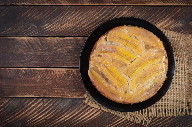 Tarta o pastel de caramelo de plátano en un plato negro sobre un fondo de madera. Vista superior, arriba