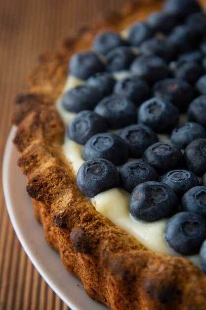 Tarta o torta del arándano con crema y bayas. Comida casera, fondo de madera, rústico.