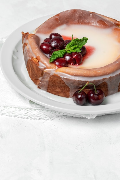 Tarta de queso casero con cerezas y menta sobre fondo blanco.