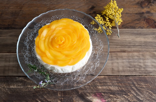 Tarta de queso con decoración de melocotones y flores amarillas sobre fondo de madera. Copie el espacio.