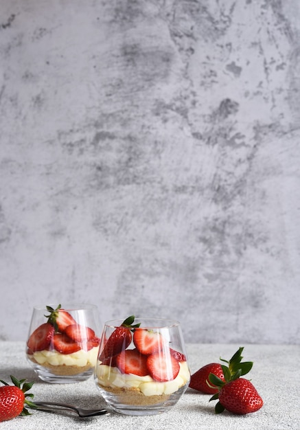 Tarta de queso con fresas en un vaso sobre una superficie de piedra clara