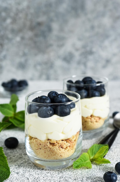 Tarta de queso con galletas y bayas en un vaso sobre un fondo de hormigón claro.