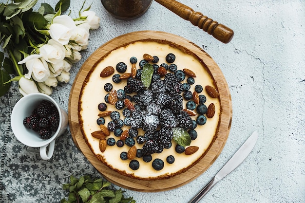 Tarta de queso con moras, almendras, fresas en el fondo blanco con servilletas y flores.