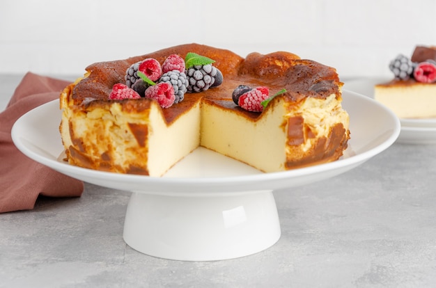 Tarta de queso de San Sebastián con frutos rojos y hojas de menta encima sobre un plato blanco sobre un fondo de hormigón gris. Postre tradicional español. Copie el espacio.