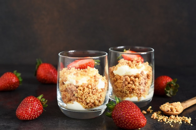 Tarta de queso en un vaso con fresas sobre un fondo de hormigón oscuro. Postre en vaso.