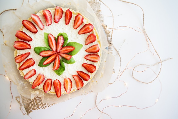 Tarta de queso de verano muy hermosa decorada con fresas - se encuentra en una mesa de madera blanca, vista superior