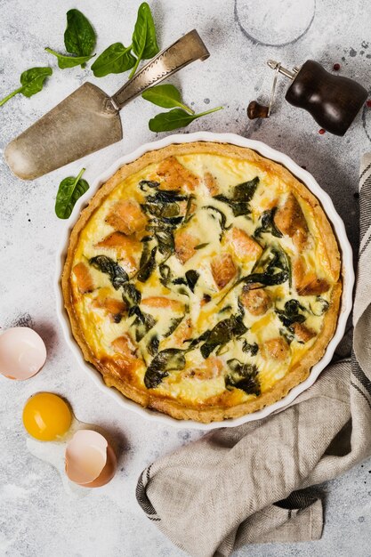 Tarta de quiche casera con pescado rojo y espinacas sobre superficie de madera clara