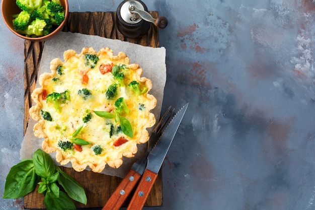 Tarta de quiche casera con salmón de pescado rojo, brócoli, albahaca, condimentos y queso sobre una mesa de piedra gris. Enfoque selectivo Vista superior.