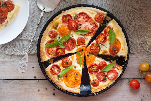 Tarta de tomate hecha con masa de hojaldre, tomates rojos y amarillos, queso y crema. Concepto de alimentación saludable o comida vegetariana sobre fondo de madera rústica