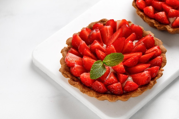 Tarta con trozos de fresa con crema de vainilla en pizarra blanca y fondo blanco de cerca Copiar espacio