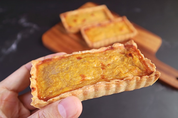 Tartaleta de calabaza deliciosa en mano con tartaletas borrosas en una placa de madera