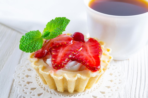 Tartaleta con fresas frescas y queso crema, y una taza de té y galletas pequeñas.