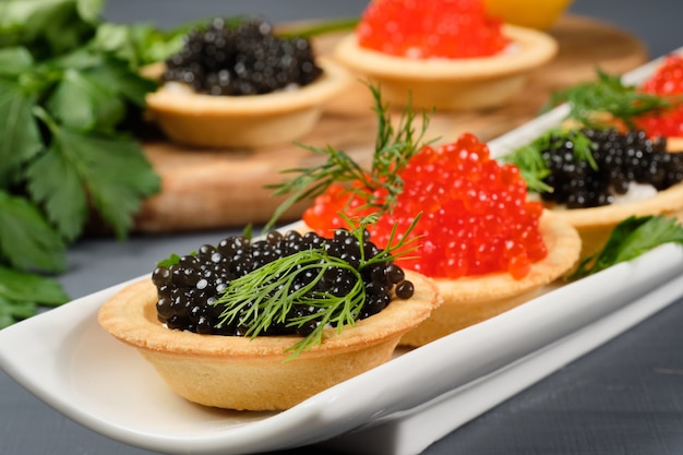 Tartaletas con caviar rojo y negro en un plato blanco con limón.