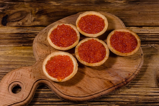 Tartaletas con caviar rojo sobre una tabla de cortar de madera. Comida festiva