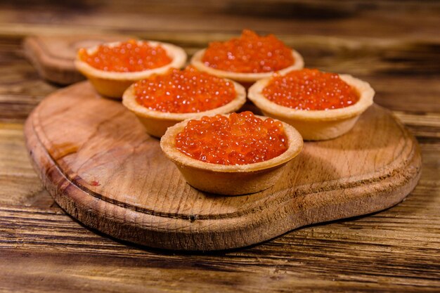 Tartaletas con caviar rojo sobre una tabla para cortar madera. comida festiva