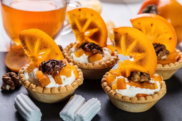 Tartaletas con crema de cuajada, caqui y té en taza transparente.