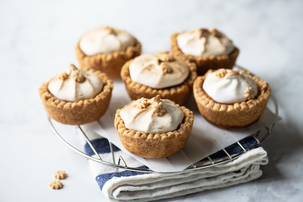 Tartaletas de cuajada de limón con merengue batido en una rejilla de alambre sobre un fondo gris