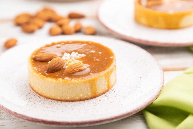 Tartaletas dulces con crema de almendras y caramelo con taza de café sobre un fondo de madera blanca y textil verde. vista lateral, primer plano, enfoque selectivo.